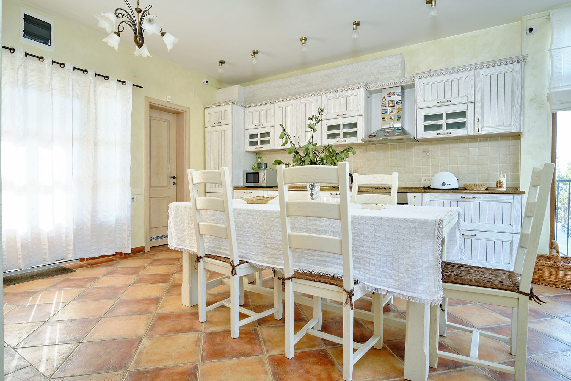 Bright kitchen-dining room in a townhouse, Bigovo, Montenegro: white furniture, dining table, and tiled floor in the interior.