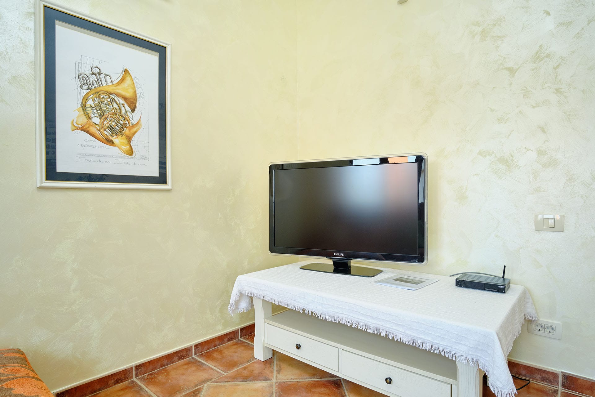 Philips TV on a white stand in the living room of a townhouse in Bigovo, Montenegro, with decorative plaster on the walls.