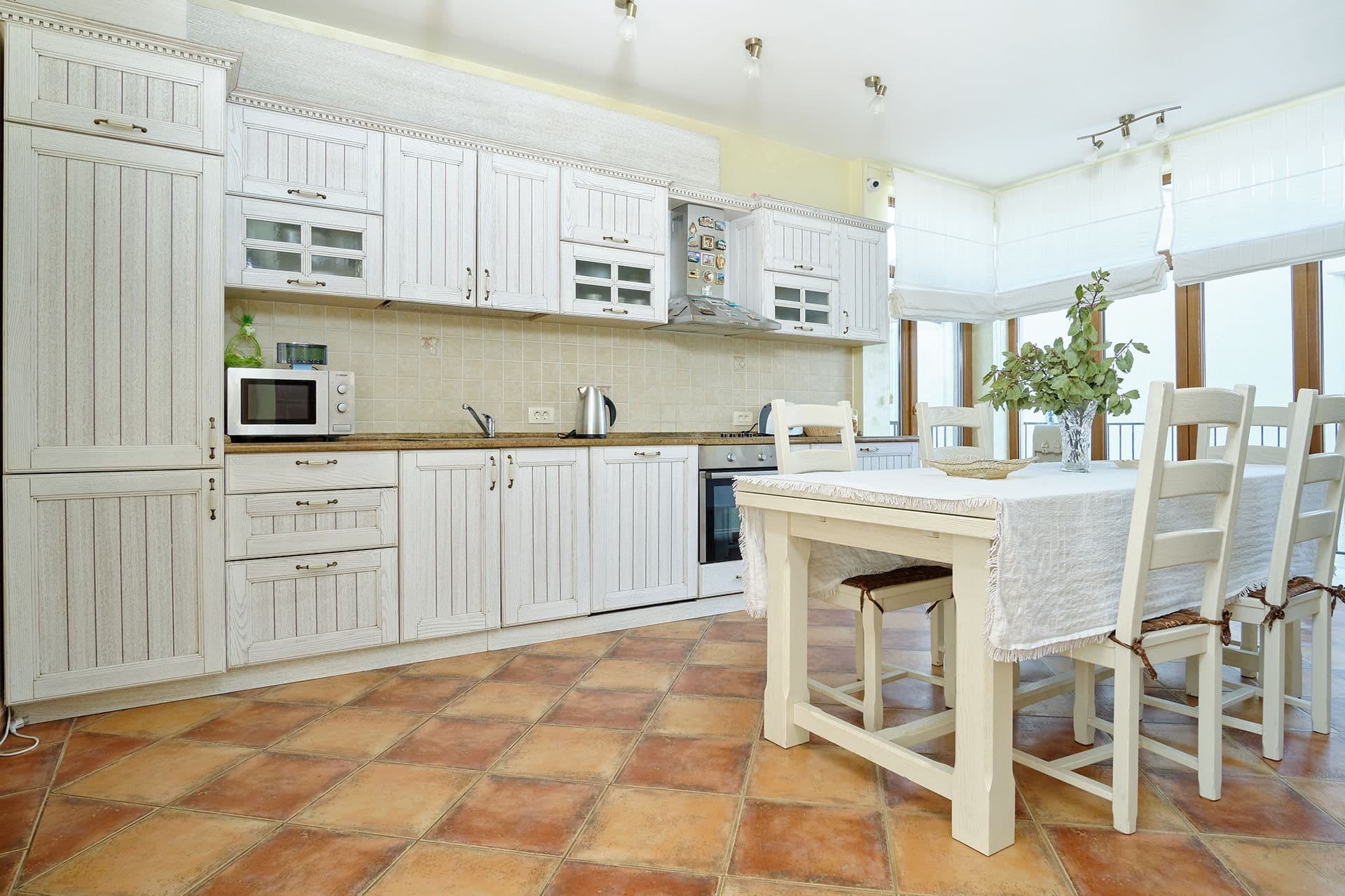 Bright kitchen in a townhouse, Bigovo, Montenegro: white Provence-style furniture, dining area, and tiled floor.