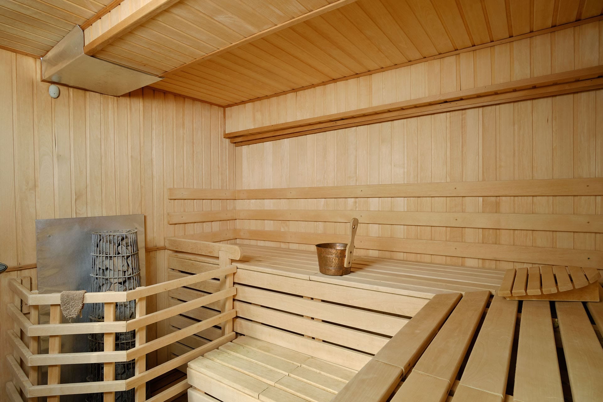 Finnish sauna with light wood finish in a townhouse, Bigovo village, Montenegro: benches, stove and ladle.