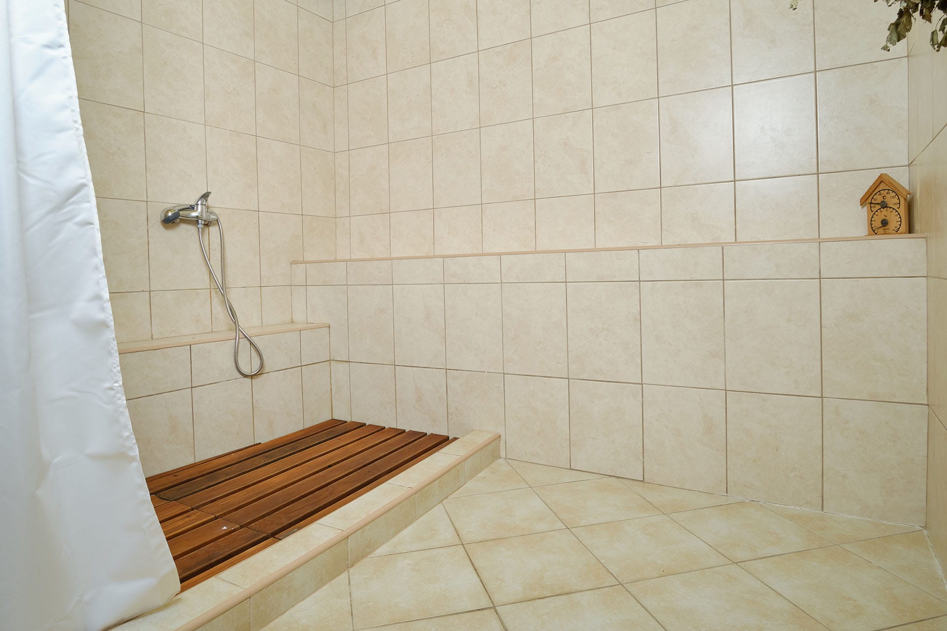Shower area in a townhouse in Bigovo, Montenegro: light tile, wooden decking, and a built-in sauna thermometer.