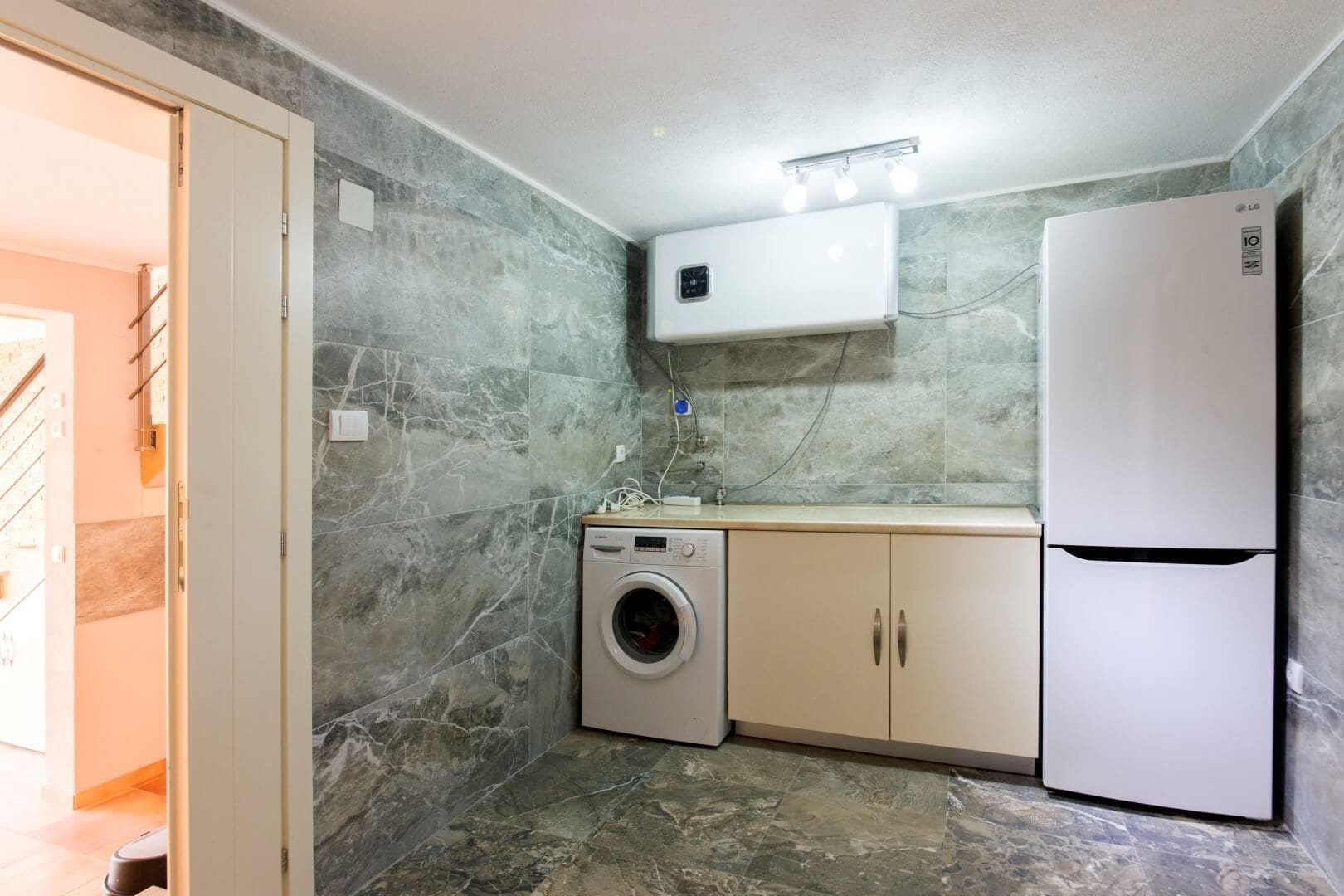 Utility room finished in gray marble, with a washing machine and refrigerator in a villa in Krašići, Montenegro.