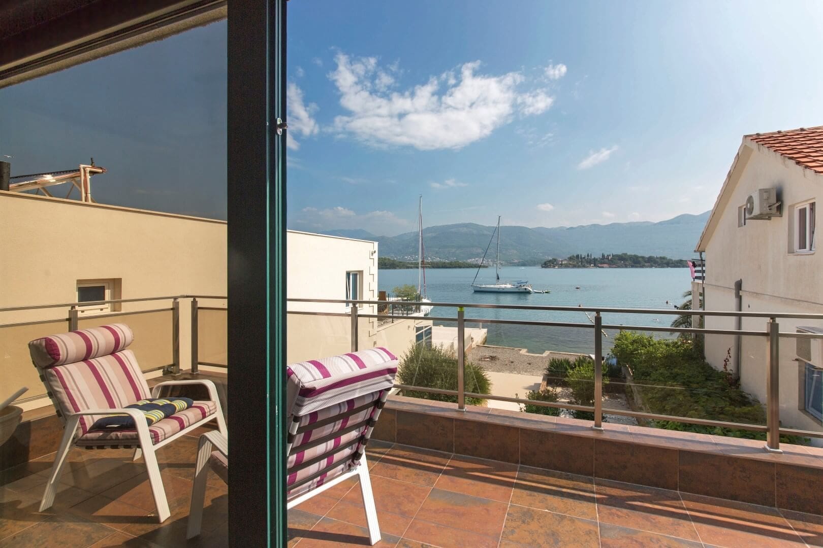 View from the villa balcony in Krašići, Montenegro: a terrace with furniture, panoramic views of the sea, mountains, and yachts in the bay.