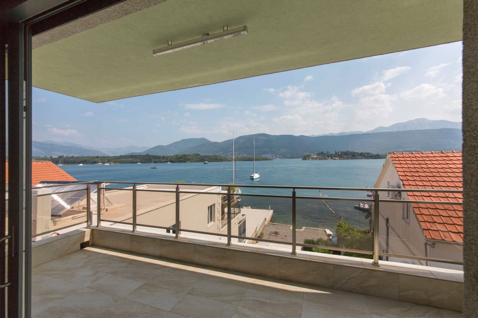 Villa balcony in Krašići, Montenegro: panoramic view of the sea, mountains, and yachts, with modern tile finish and railings.