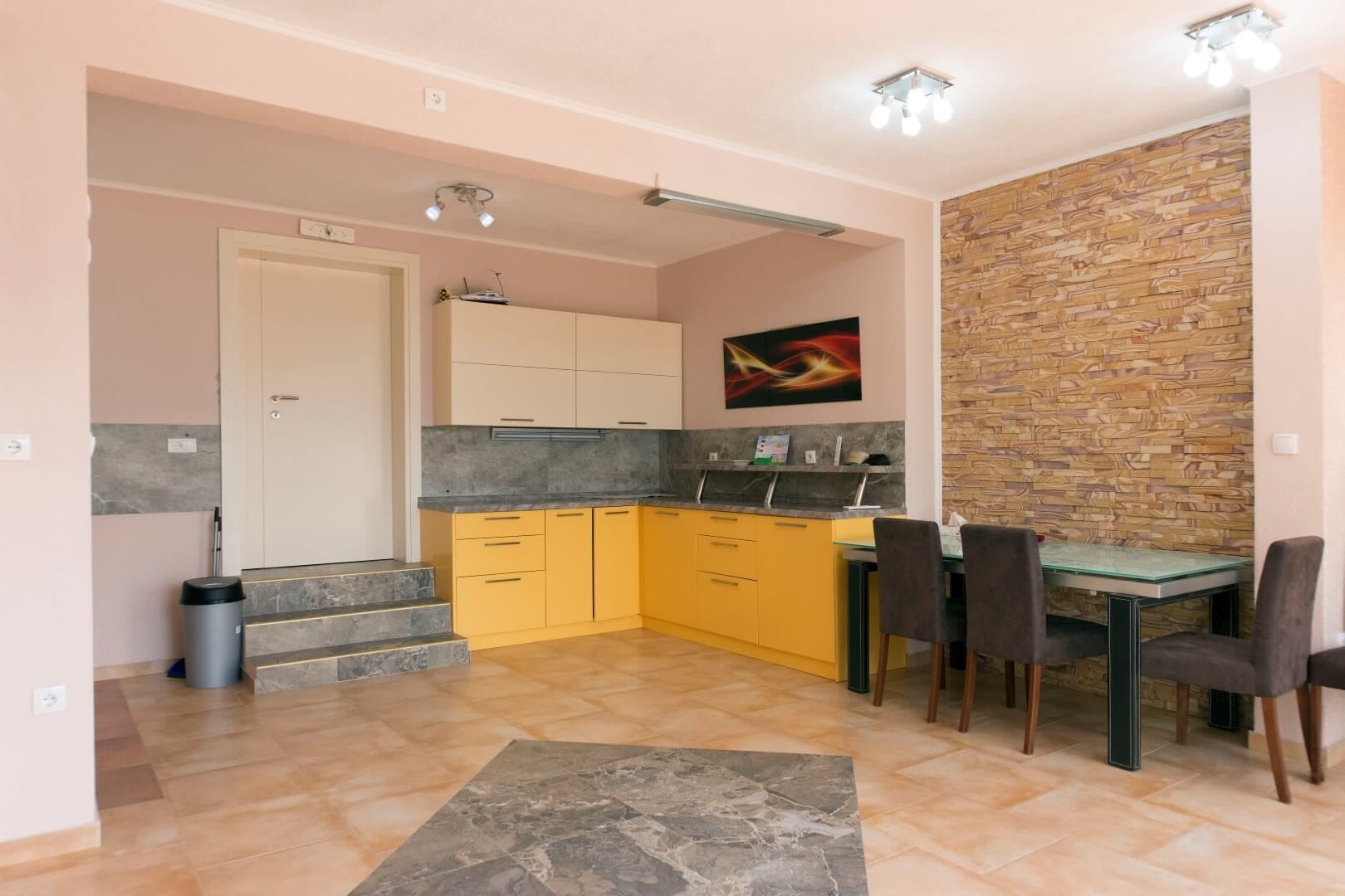 Kitchen with a yellow cabinet set and dining area in a villa in Krašići, Montenegro: stone wall finish and tiled floor.