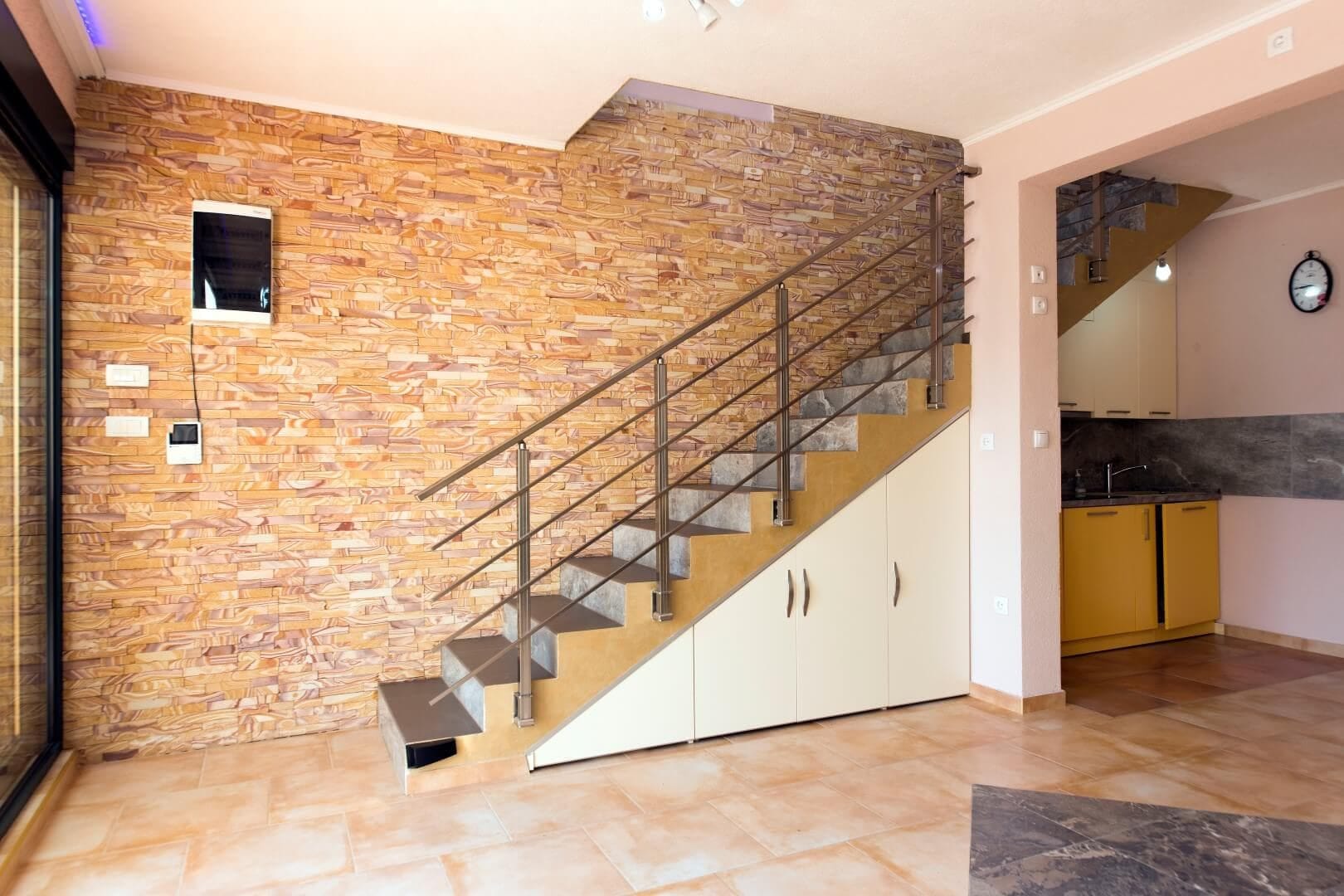 Living room interior with a stone wall and staircase in a villa, Krašići, Montenegro: built-in cabinets and modern finishes.