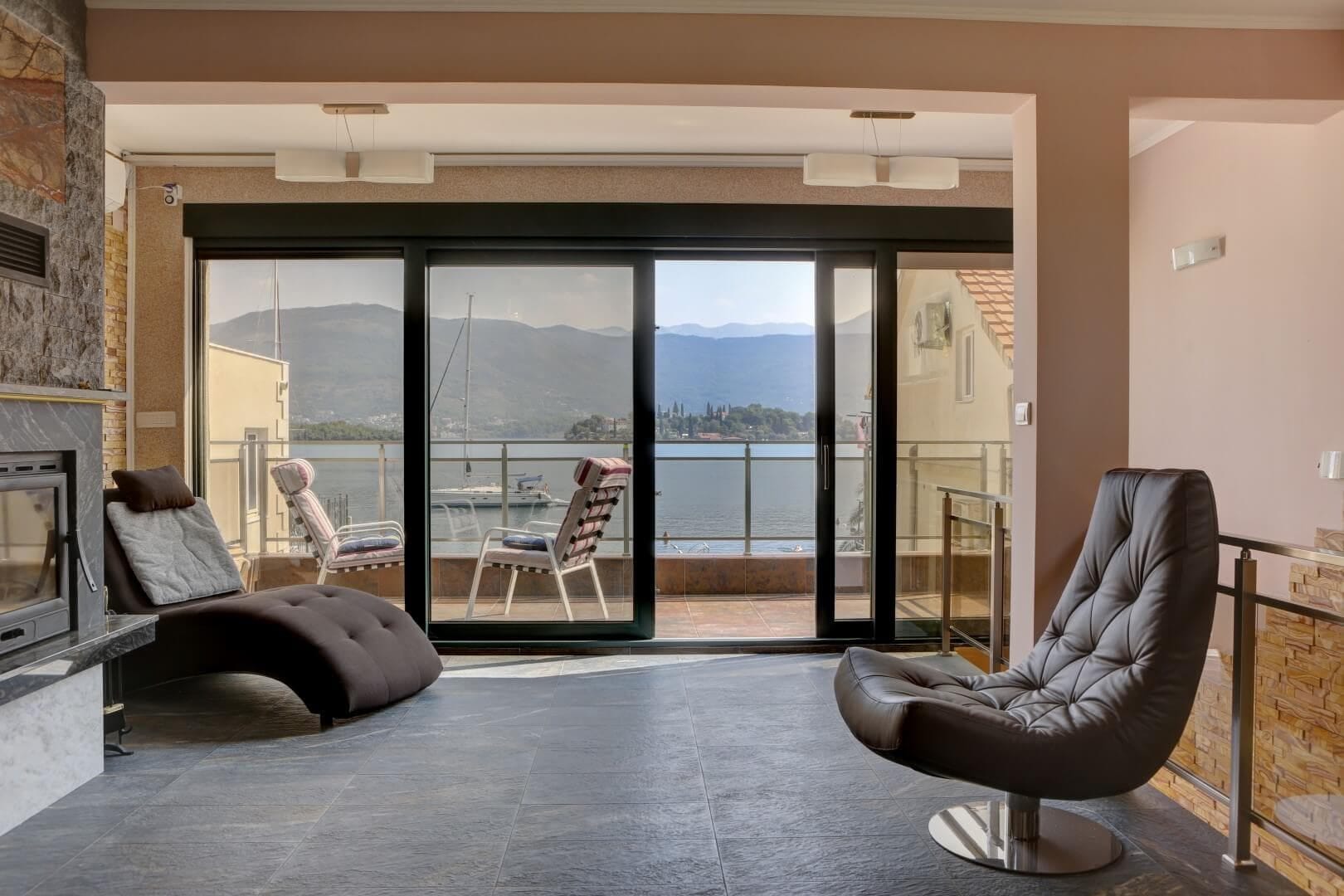 Living room with a fireplace and panoramic sea view in a villa, Krašići, Montenegro: stylish furniture and access to the terrace.