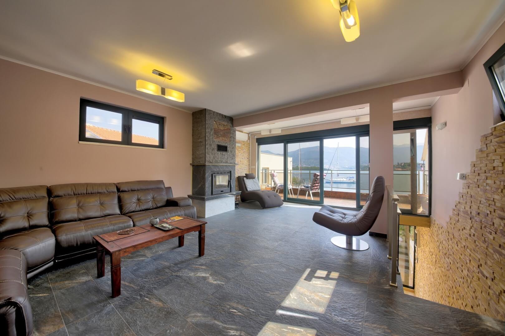 Living room with a fireplace and leather furniture in a villa in Krašići, Montenegro, with panoramic views of the sea and yachts.