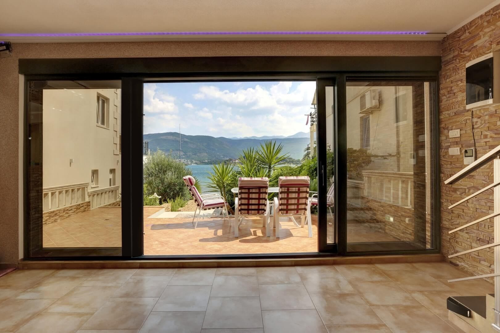 Villa living room in Krašići, Montenegro: panoramic windows, access to a terrace with sea and mountain views, tiled floor.