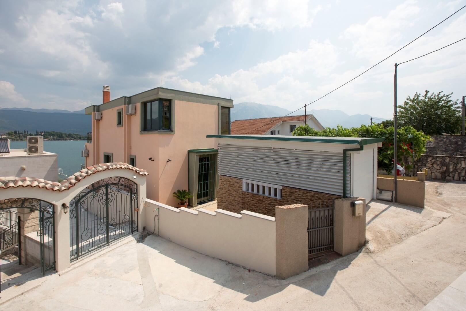 Villa in Krašići, Montenegro: house facade with a garage, wrought-iron gates, and panoramic sea and mountain views.