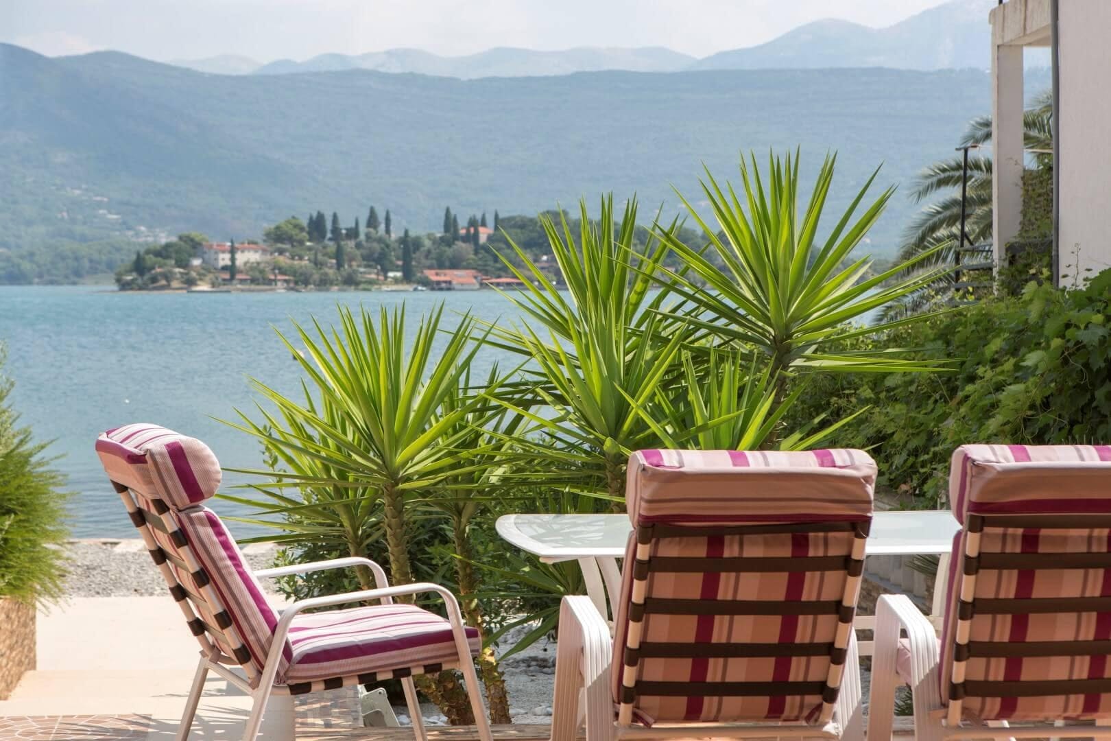 Villa terrace in Krašići, Montenegro: sea and mountain views, garden furniture, palm trees, and direct access to the coast.
