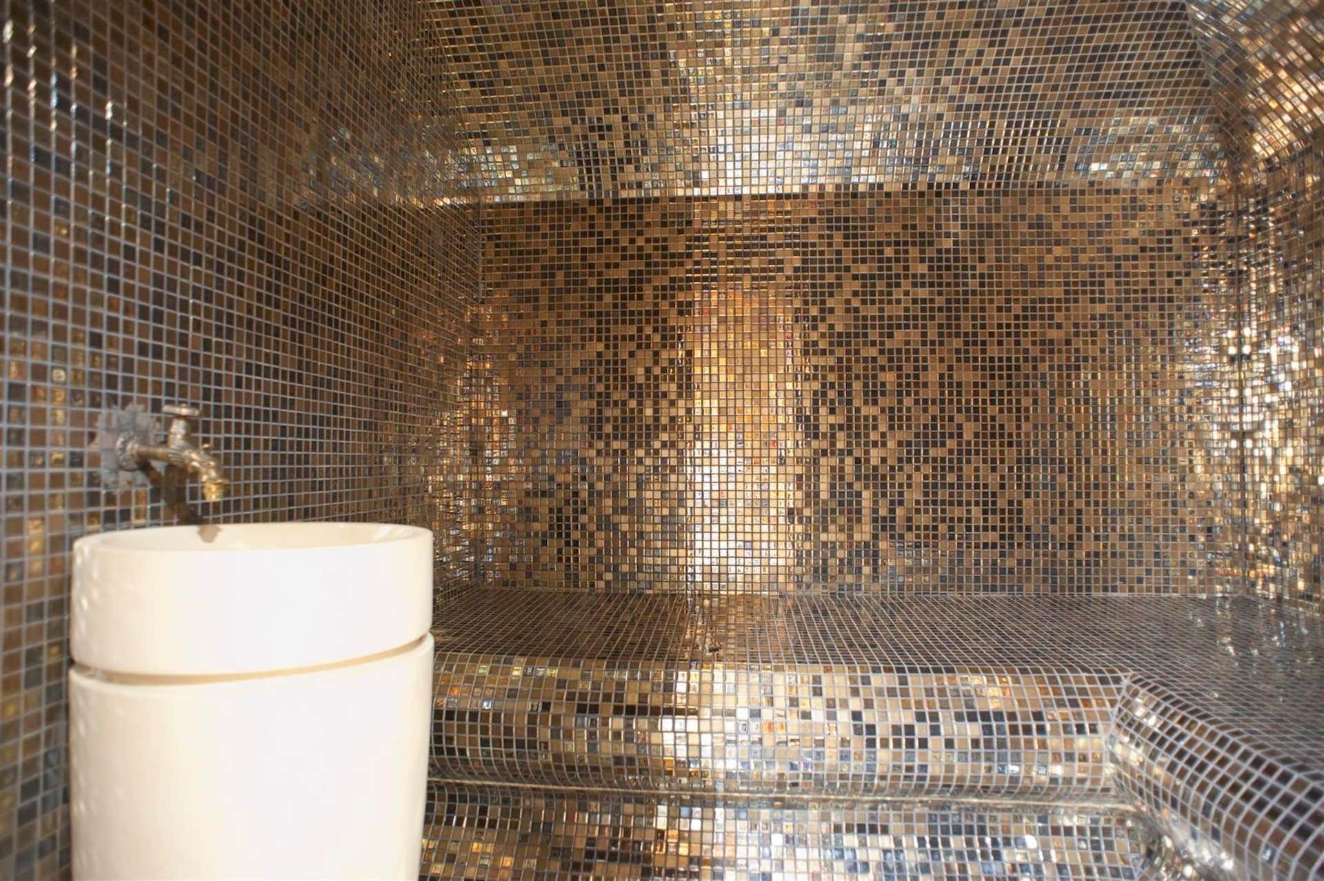 Designer bathroom with gold mosaic finishes and a white sink in a villa in Krašići, Montenegro.