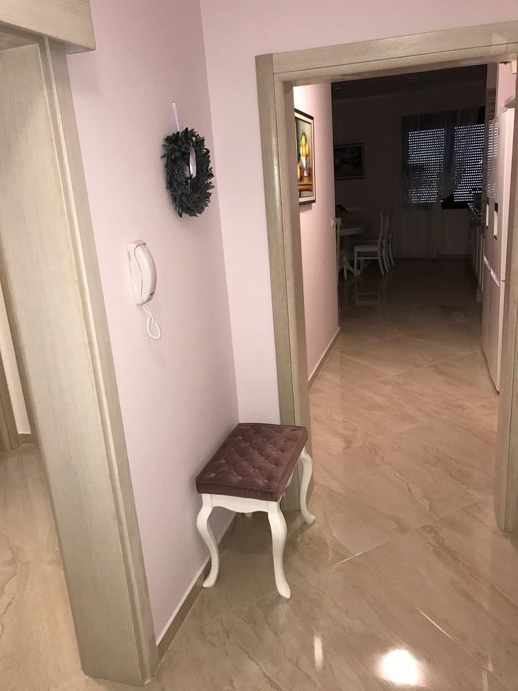 Hallway with a soft ottoman and light finishes in an apartment, Dobrye Vody, Montenegro. View of the living room with tile flooring.