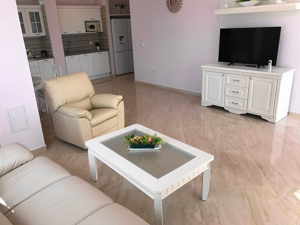 Bright living room with kitchen in an apartment in Dobri Vody, Montenegro: white furniture, leather armchair, and marble floor.