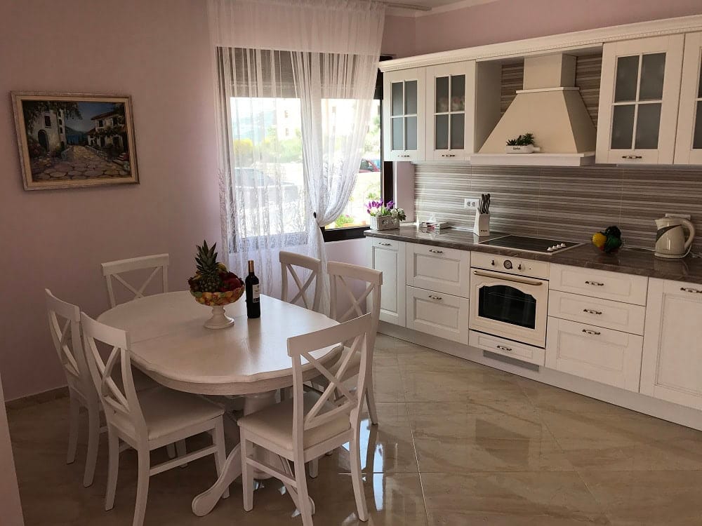 Bright kitchen-dining room with white furniture in an apartment in Dobri Vody, Montenegro: dining table and modern appliances.
