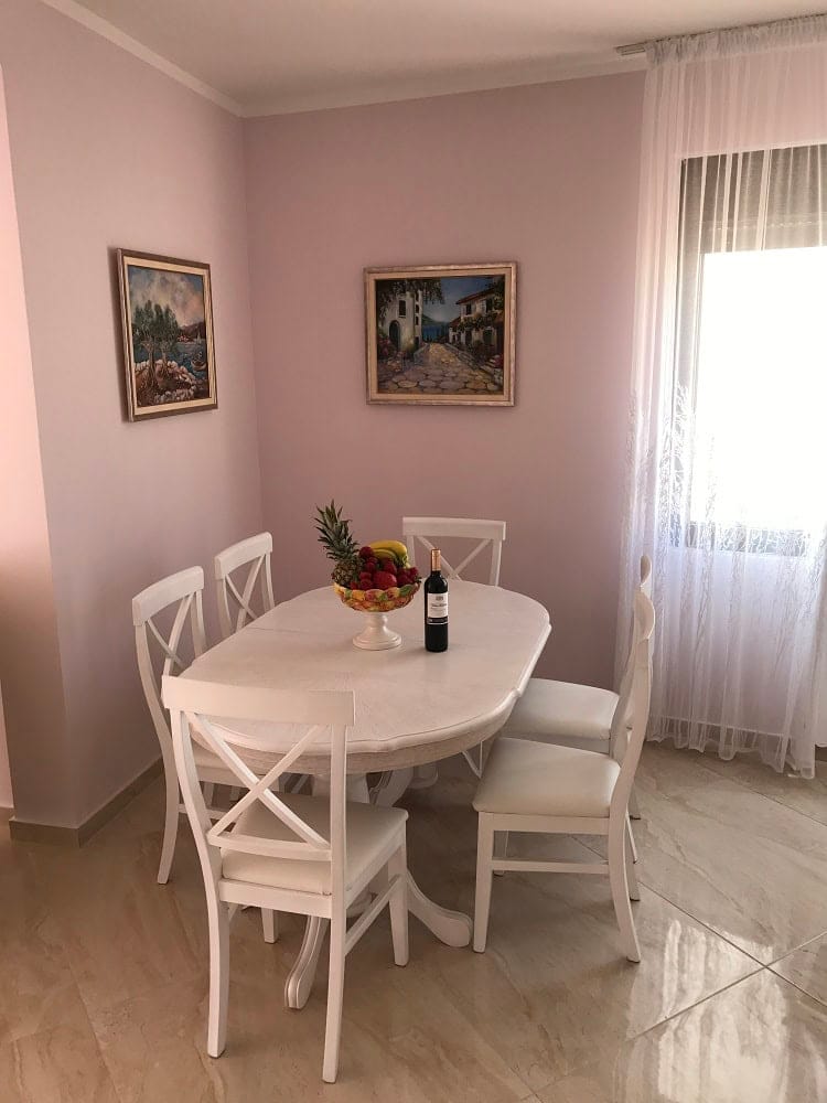 Dining area with a white table and chairs in an apartment, Dobri Vody, Montenegro. Bright interior with paintings on the walls.