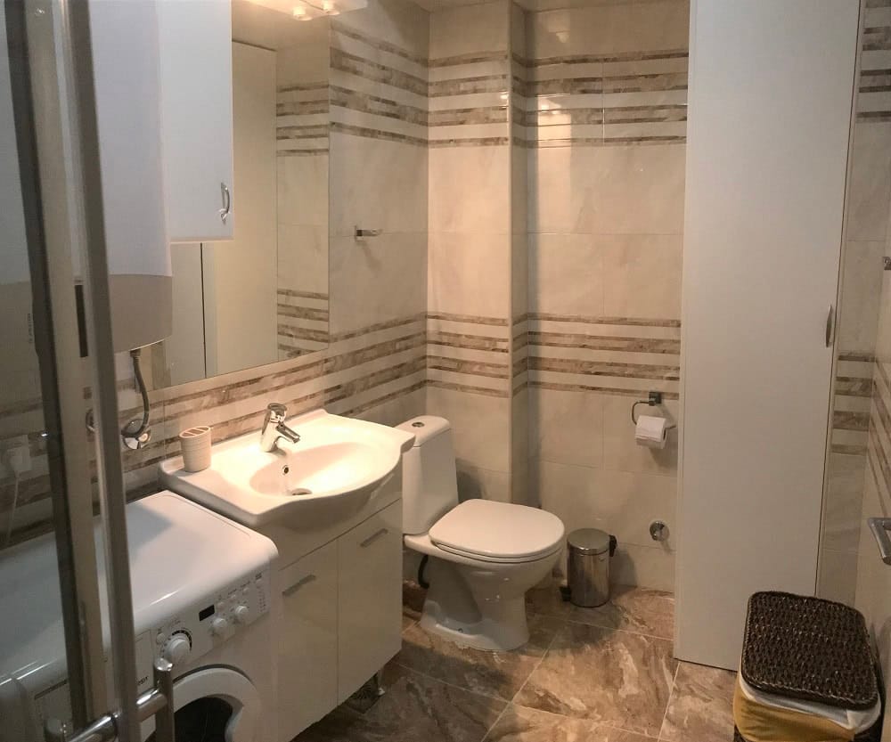 Modern bathroom in an apartment in Dobrih Voda, Montenegro: light tiles, a sink with vanity, and a washing machine.