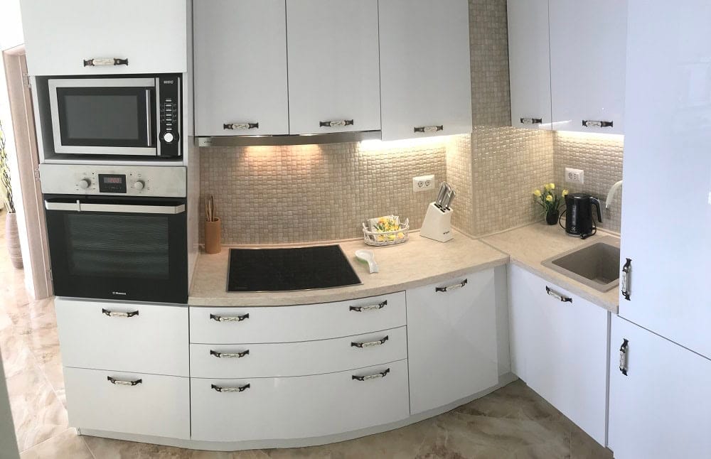 Modern white kitchen in an apartment in Dobrih Voda, Montenegro: built-in appliances, mosaic backsplash, and stone countertop