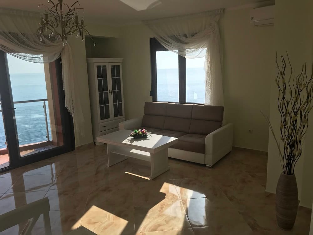 Living room with sea view in an apartment, Dobrye Vody, Montenegro: light furniture, panoramic windows, and tiled floor.