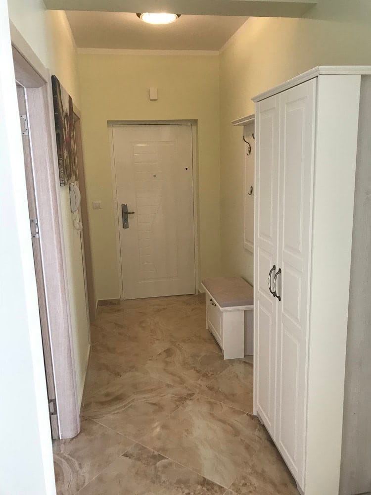 Bright entryway in an apartment, Dobrota, Montenegro: white wardrobe, bench, and tiled floor in the interior.