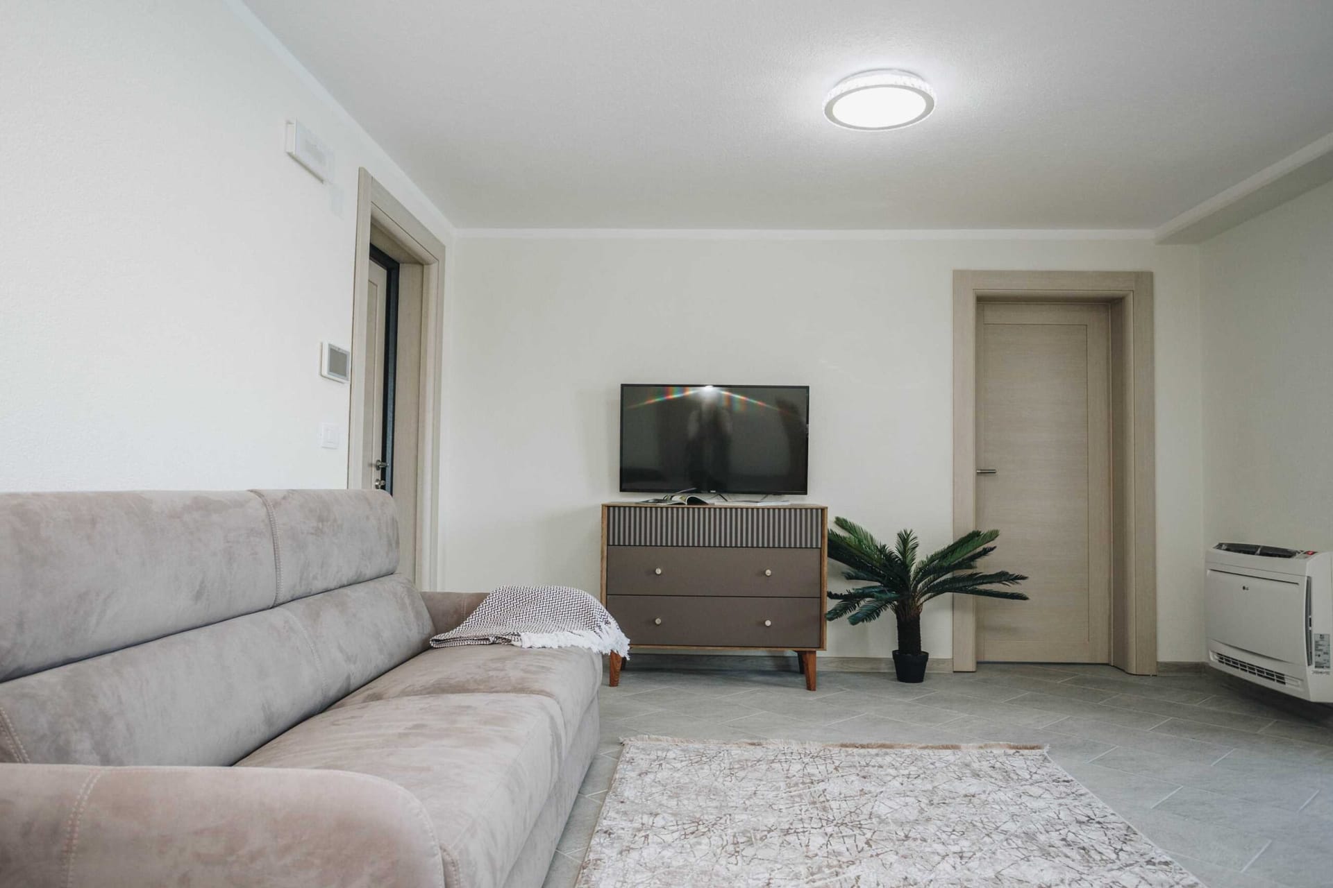 Bright living room with a gray sofa and TV area in a villa in Krašići, Montenegro: modern interior with tiled flooring.