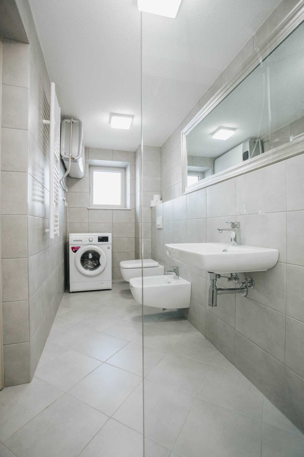 Modern bathroom with a shower and washing machine in a villa in Krašići, Montenegro. Light-colored tiles and fixtures.