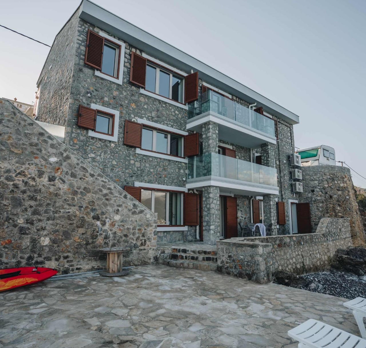 Facade of a stone villa in Krašići, Montenegro: terrace, glass balconies, and wooden shutters by the sea.