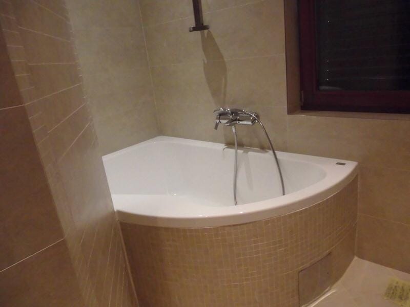 Bathroom in an apartment in Petrovac, Montenegro: corner bathtub with beige mosaic finish and chrome faucet.
