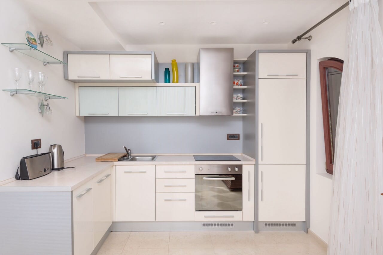 Modern bright kitchen in an apartment in Petrovac, Montenegro: built-in appliances, white fronts, and glass shelves.