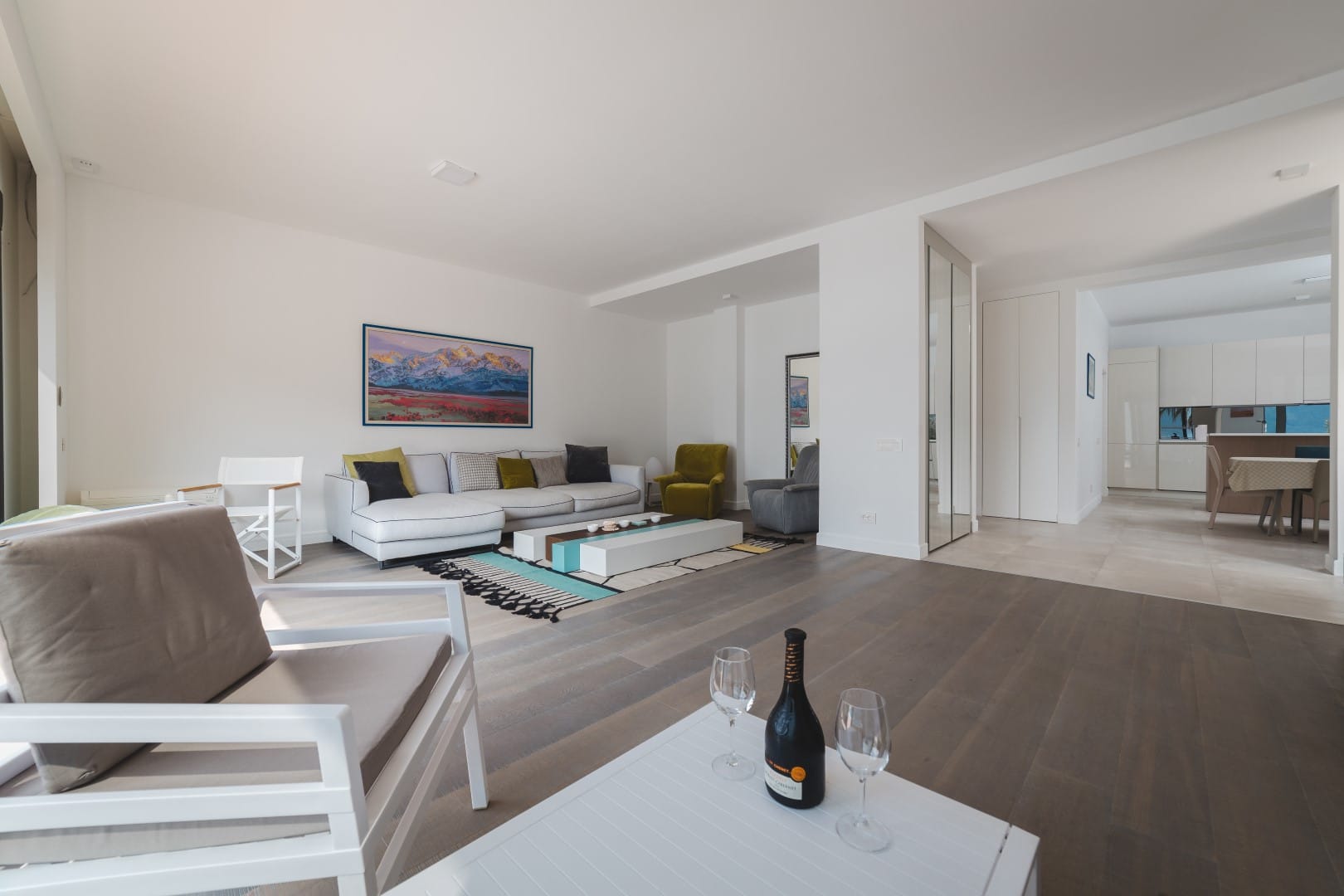 Modern living room with a white sofa and kitchen in a villa in Strp, Montenegro: stylish interior, parquet flooring, and sea view.