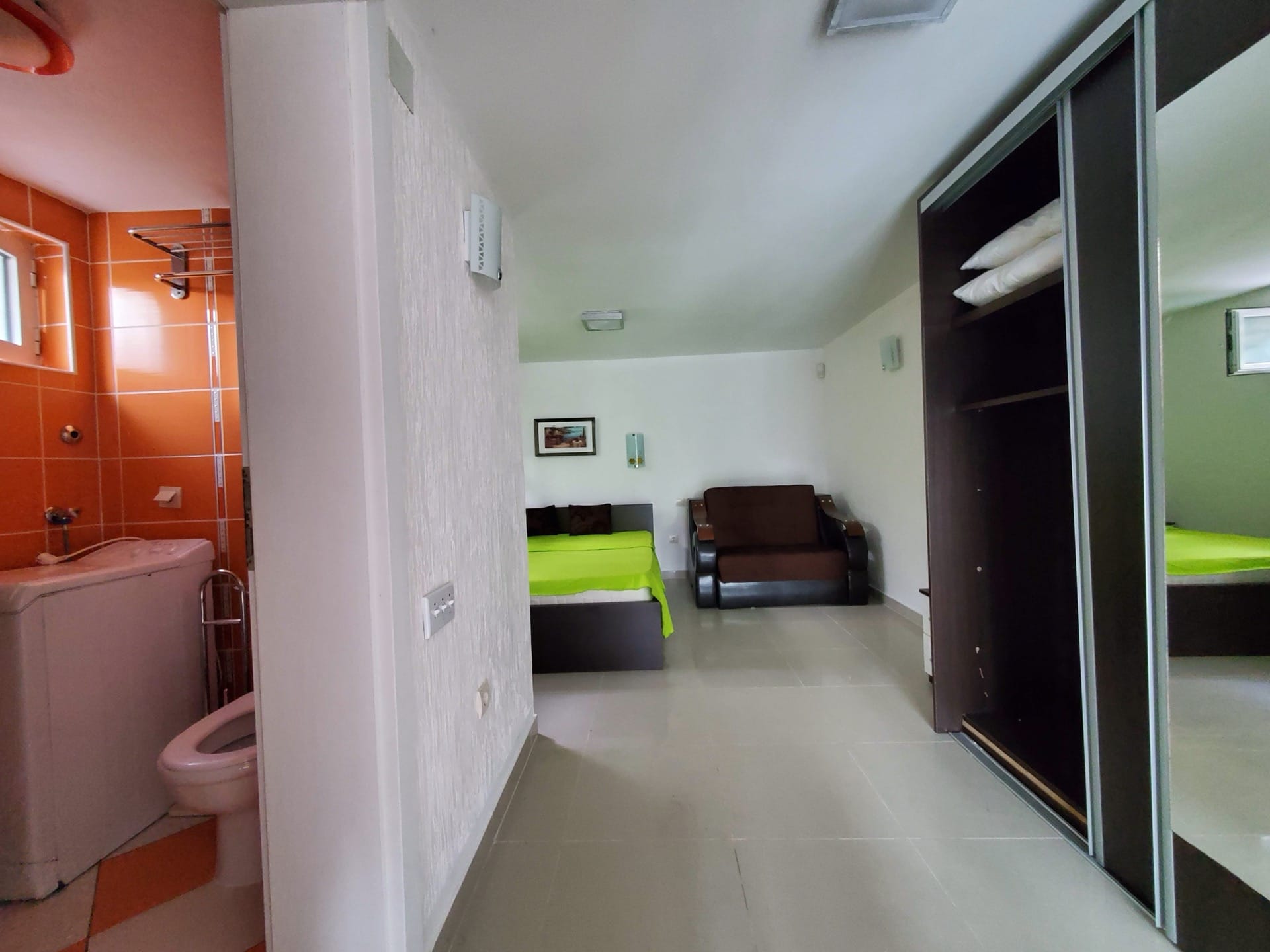 Hotel room interior in Bijela, Montenegro: bedroom with a bed, sofa, wardrobe, and a bathroom with orange tiles.