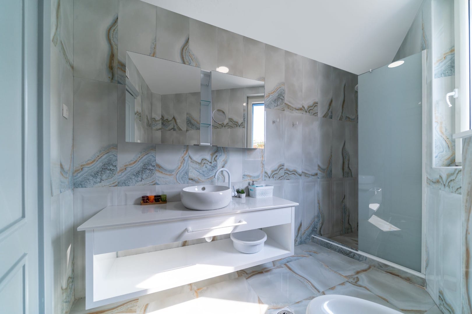 Modern bathroom with marble-look finishes in a house, Blizikuće, Montenegro: white vanity, sink, and shower cabin.