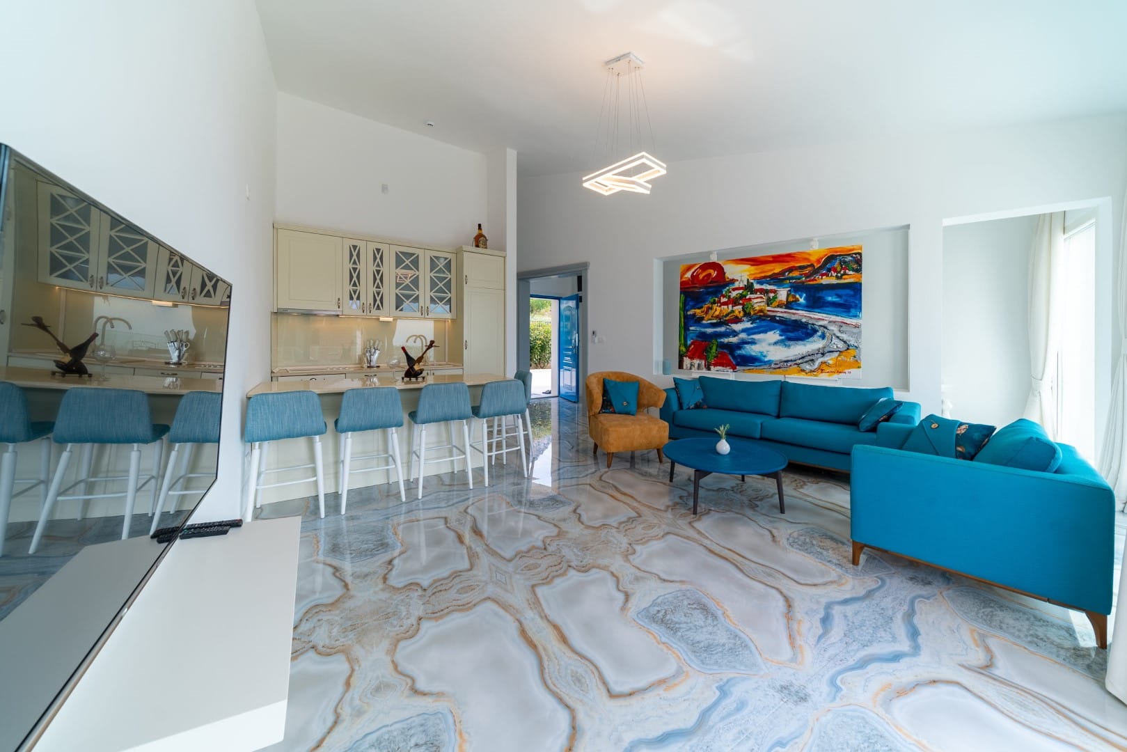 Living room with marble floor, blue furniture, and kitchen in a house, Blizikuće, Montenegro. Modern interior with a bright painting.