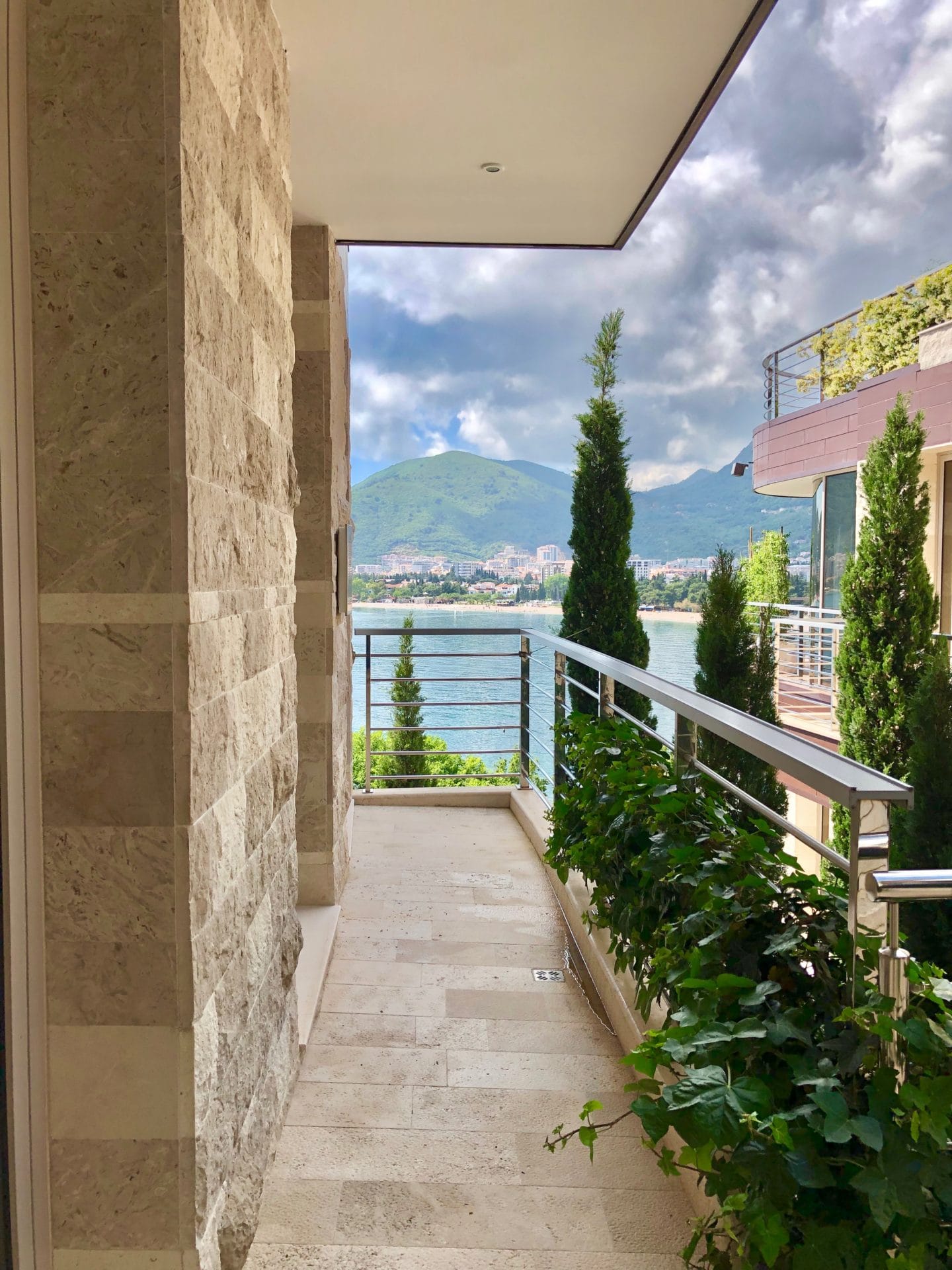 Apartment balcony in Budva, Montenegro: stone finishes, sea and mountain views, greenery, and modern railing.
