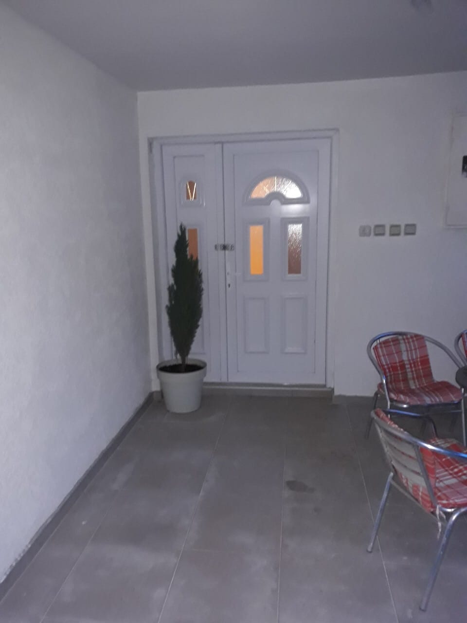 Entrance to the house in Zhanitsa, Montenegro: white double door, tiled terrace, chairs, and a decorative plant.