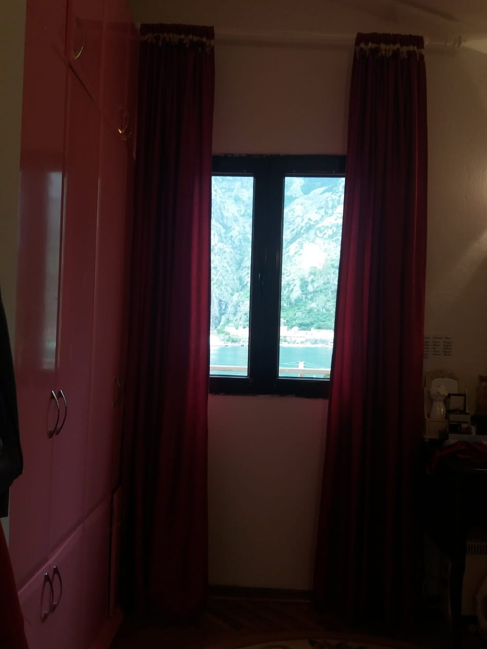 Bedroom with red curtains and a view of Kotor Bay and the mountains in a house in Muo, Montenegro.