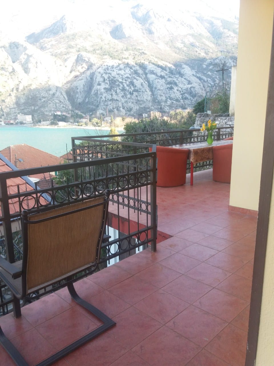 Terrace with furniture and views of Kotor Bay and the mountains in a house, Muo, Montenegro. Tiled floor and wrought-iron railings.