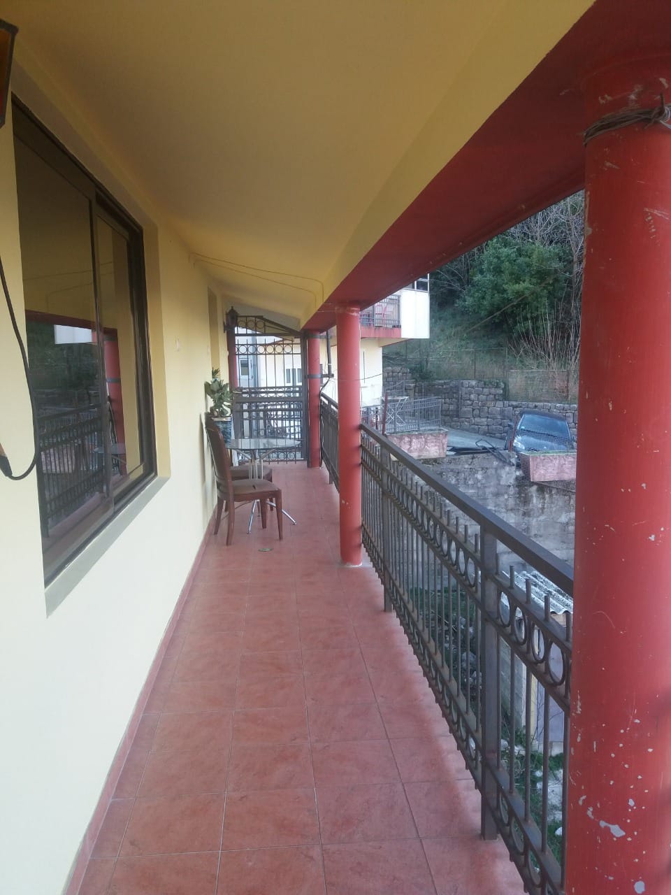 Spacious balcony with red columns and furniture in a house, Muo, Montenegro: view of the terrace and garden.