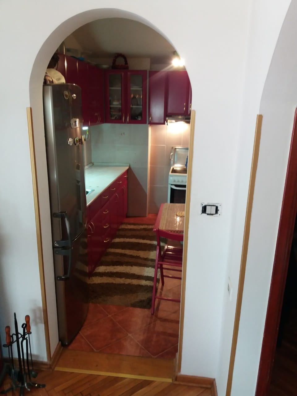 Kitchen with burgundy cabinetry and an arched doorway in a house in Muo, Montenegro: view of the cooking area and dining table.