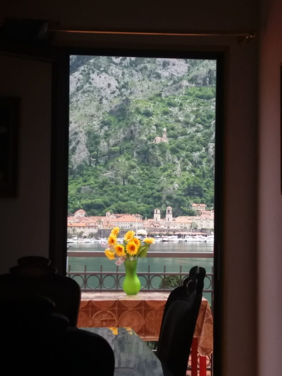View from the living room of a house in Muo, Montenegro: a panorama of the Bay of Kotor, mountains, and the old town from a terrace with flowers.