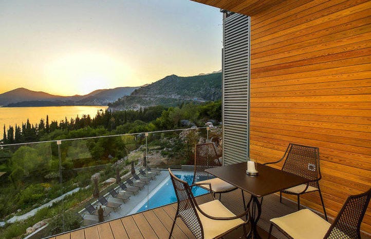 Apartment balcony in Kamenovo, Montenegro: sea, mountain, and pool view, wooden finish, table with chairs.