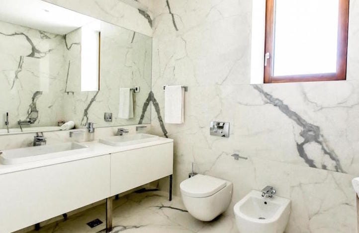 Modern bathroom with white marble finish in an apartment, Kamenovo, Montenegro: two sinks and plumbing fixtures.