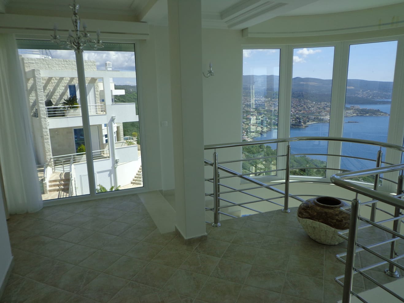 Villa living room in Dobra Voda, Montenegro: panoramic windows with sea view, bright interior, and staircase with railing.