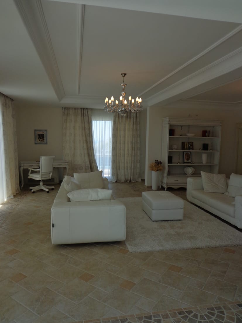 Spacious living room with white furniture and a chandelier in a villa in Dobra Voda, Montenegro: interior with stone flooring.