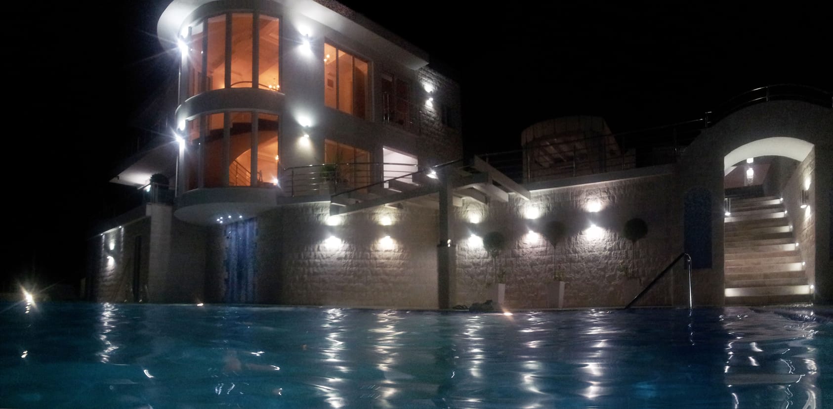 Modern villa with a pool and night lighting in Dobra Voda, Montenegro: panoramic windows and stone cladding.