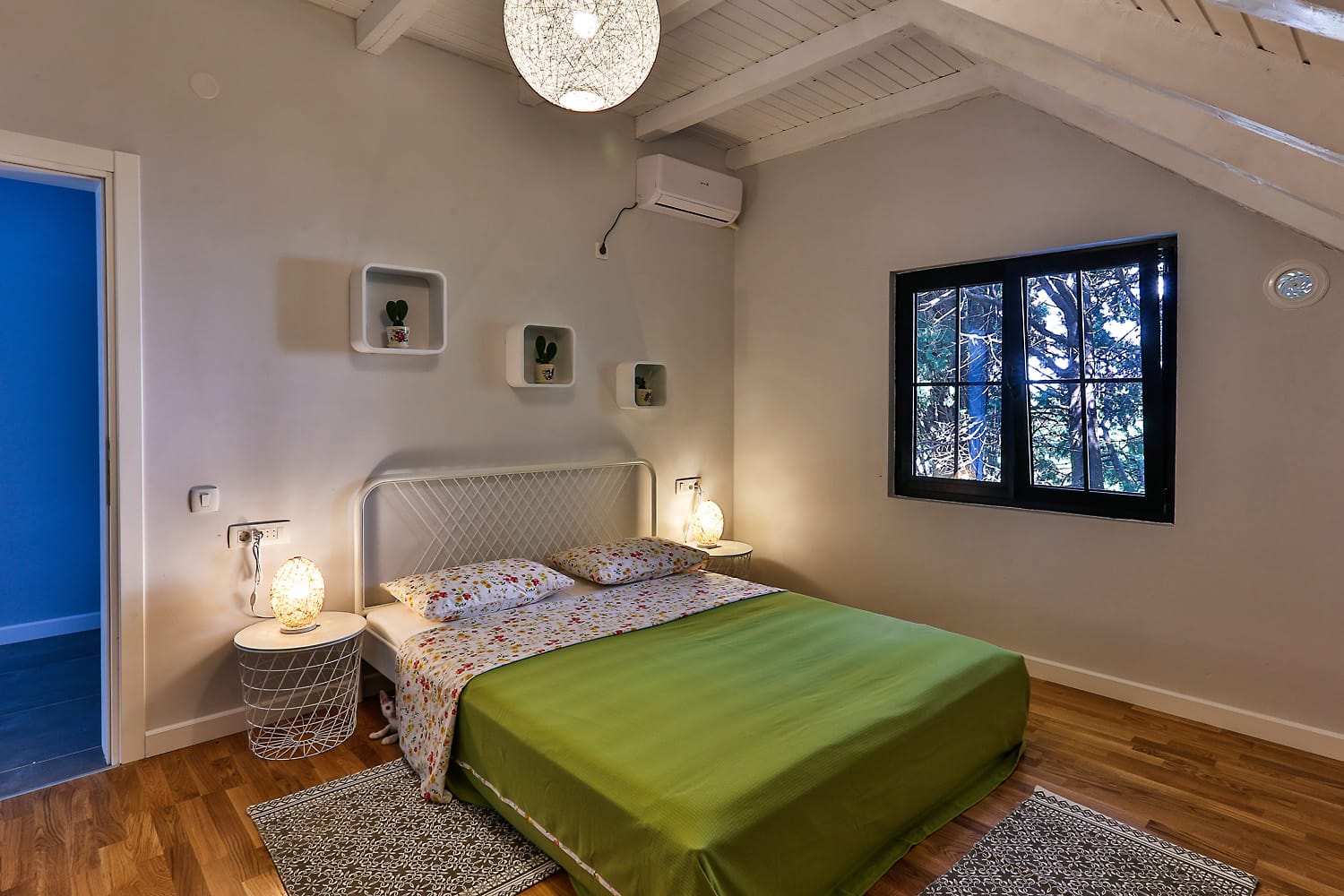 Cozy bedroom in a house in Sutomore, Montenegro: double bed, wooden floor, and a view of the garden from the window.