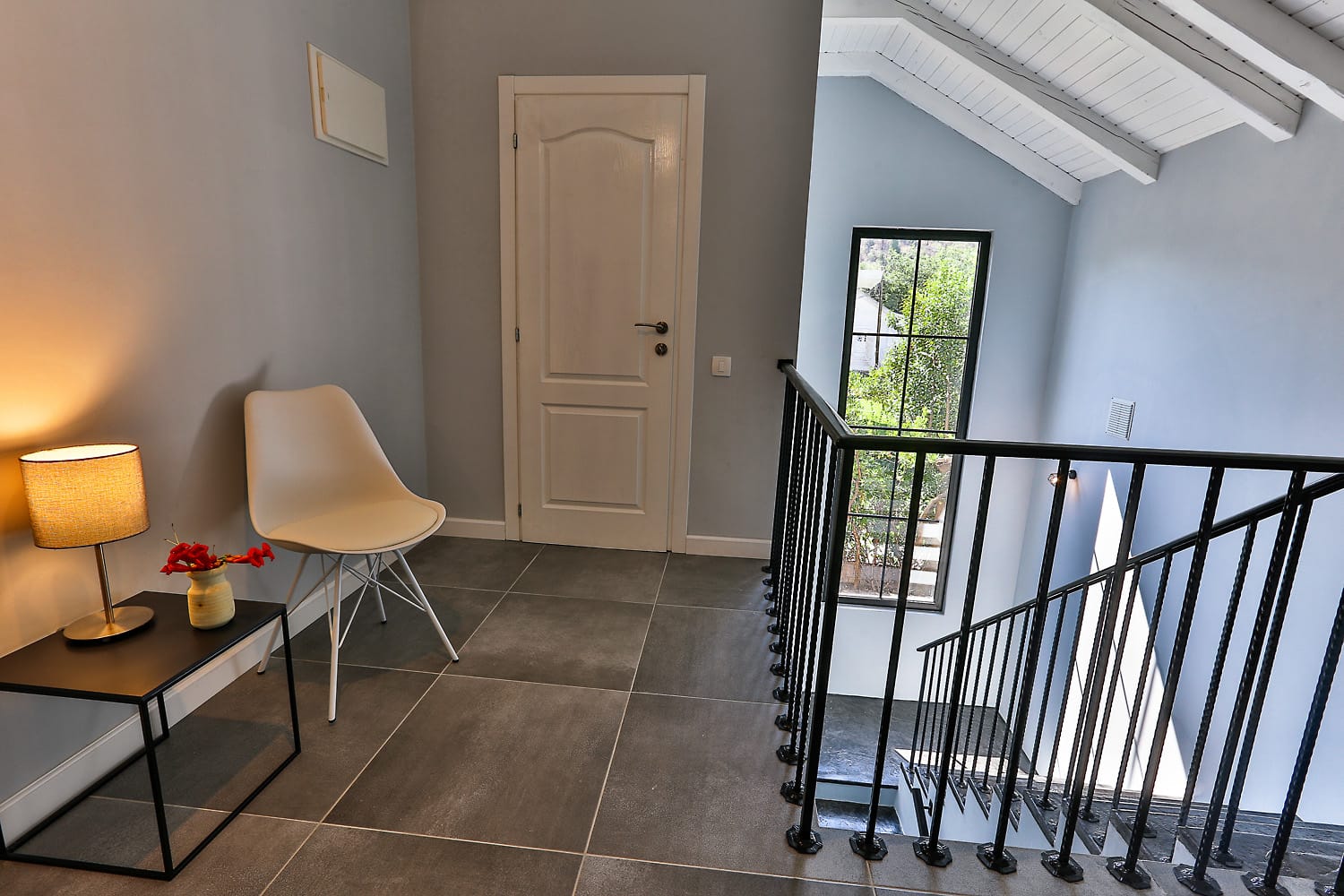 Interior of a house in Sutomore, Montenegro: staircase with wrought-iron railings, modern furniture, and a view of the garden from the window.