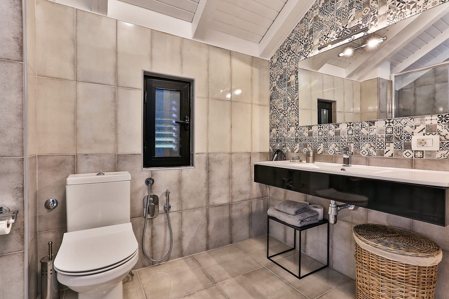 Modern bathroom with patchwork tiles in a house in Sutomore, Montenegro: stylish fixtures and a woven basket.