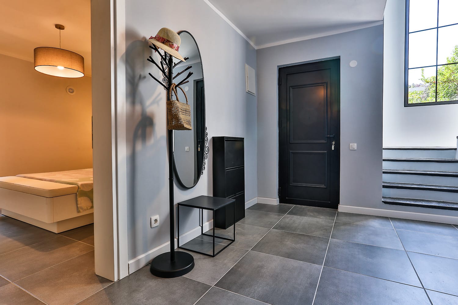 Modern hallway with a dark door and staircase in a house, Sutomore, Montenegro: stylish furniture, mirror, and tile.