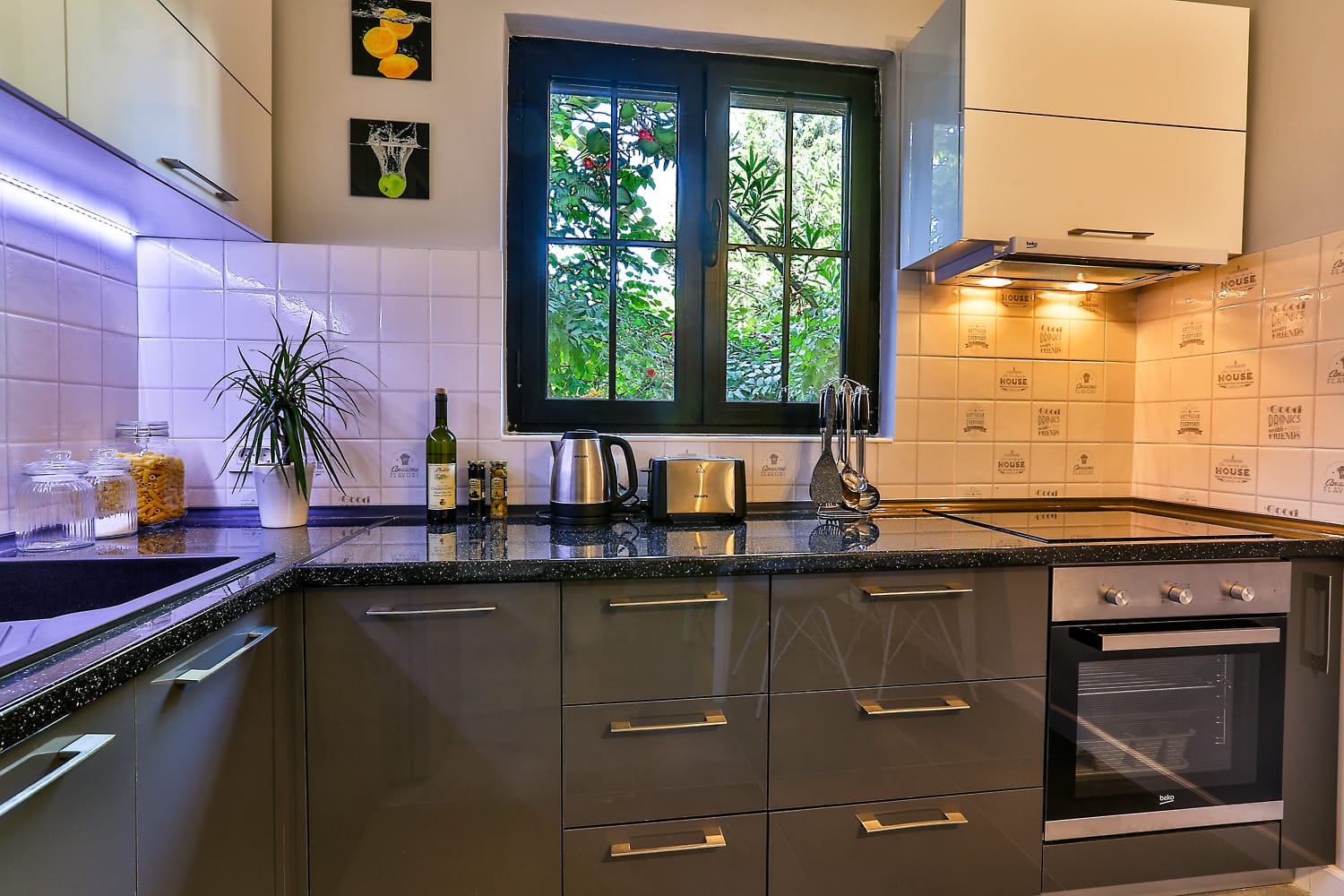 Modern kitchen in a house in Sutomore, Montenegro: glossy cabinet fronts, black countertop, and a view of greenery from the window.